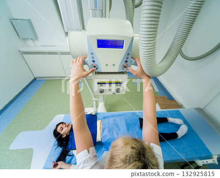Radiologist and patient in a x-ray room. Classic ceiling-mounted x-ray system. Radiologist and patient in a x-ray room. Classic ceiling-mounted x-ray system. 132925815