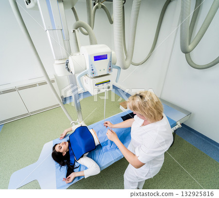 Radiologist and patient in a x-ray room. Classic ceiling-mounted x-ray system. 132925816