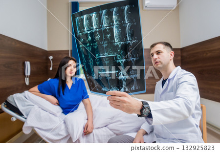 Traumatologist showing MRI film to patient in hospital. Traumatologist showing MRI film to patient in hospital. 132925823