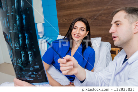 Traumatologist showing MRI film to patient in hospital. Traumatologist showing MRI film to patient in hospital. 132925825