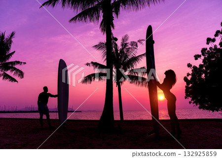 Silhouette of surfers couple holding long surf boards at sunset  132925859
