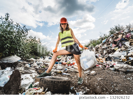 Woman volunteer helps clean the field of plastic garbage and old tires.  132926232