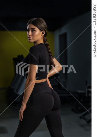 female athlete stands proudly with a strong posture in a gym. She wears black activewear and has a focused expression. female athlete stands proudly with a strong posture in a gym. She wears black activewear and has a focused expression. 132926958