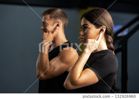 man and woman wear headphones as they listen to music. They focus on their workout demonstrating fitness and teamwork in their routine. man and woman wear headphones as they listen to music. They focus on their workout demonstrating fitness and teamwork in their routine. 132926960