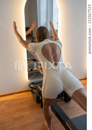 Woman training pilates on the reformer bed. Reformer pilates studio machine for fitness workouts in gym. Fit, healthy and strong authentical body. Fitness concept 132927525
