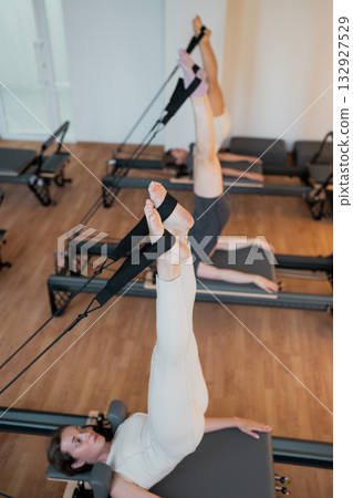 Woman lying on reformer performs controlled leg circles emphasizing core engagement and therapeutic. 132927529