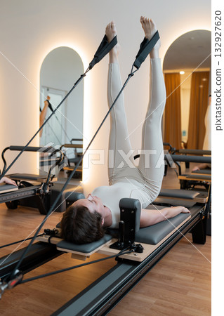 Pilates core focus, reformer movement with calm lighting, woman performs controlled leg circles Pilates core focus, reformer movement with calm lighting, woman performs controlled leg circles 132927620