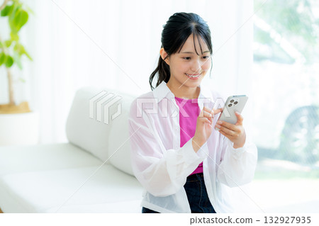 A young woman operating a smartphone in a room A young woman operating a smartphone in a room 132927935