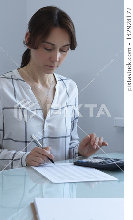 A professional woman calculates finances, checks documents, and accurately and carefully tracks business expenses at a glass table. Audit and taxes in business. A professional woman calculates finances, checks documents, and accurately and carefully tracks business expenses at a glass table. Audit and taxes in business. 132928172