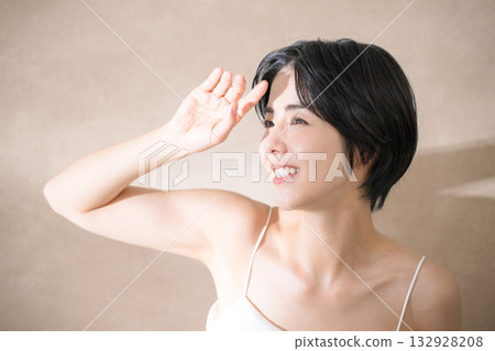 A woman who is concerned about the sunlight and is dazzled by it against a pink beige background. Close-up image of UV rays, the sun, and sunscreen. A woman who is concerned about the sunlight and is dazzled by it against a pink beige background. Close-up image of UV rays, the sun, and sunscreen. 132928208