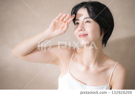 A woman who is concerned about the sunlight and is dazzled by it against a pink beige background. Close-up image of UV rays, the sun, and sunscreen. A woman who is concerned about the sunlight and is dazzled by it against a pink beige background. Close-up image of UV rays, the sun, and sunscreen. 132928209