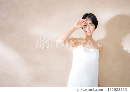 A woman who is concerned about the sunlight and is dazzled by it against a pink beige background. Image of UV rays, the sun, and sunscreen. 132928213