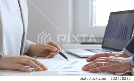 Financial analysts reviewing laptop screen and printed documents, pointing at data charts and discussing investment strategies together in modern office setting. Business people concept Financial analysts reviewing laptop screen and printed documents, pointing at data charts and discussing investment strategies together in modern office setting. Business people concept 132928222