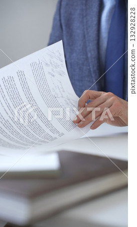 Closeup of businessman hands signing a contract with elegant pen, wearing a blue suit and a wristwatch, sitting at a white desk in office. Business people concept 132928228