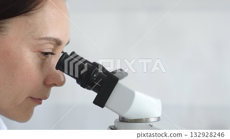 Female scientist peering into microscope, analyzing biological sample with precision in sterile laboratory research environment. Medicine and science concept Female scientist peering into microscope, analyzing biological sample with precision in sterile laboratory research environment. Medicine and science concept 132928246