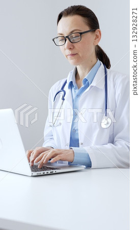 Female doctor is typing on a laptop in a bright medical office, showcasing healthcare technology and medical documentation. Medicine and health care concept Female doctor is typing on a laptop in a bright medical office, showcasing healthcare technology and medical documentation. Medicine and health care concept 132928271
