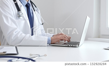 Male doctor is typing on laptop, updating electronic patient records with focused concentration, representing digital transformation in healthcare workplace. Medicine and healthcare Male doctor is typing on laptop, updating electronic patient records with focused concentration, representing digital transformation in healthcare workplace. Medicine and healthcare 132928284
