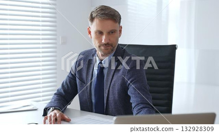 Focused mature businessman wearing suit and tie sitting at office desk and signing documents, using calculator. Audit and taxes theme in business Focused mature businessman wearing suit and tie sitting at office desk and signing documents, using calculator. Audit and taxes theme in business 132928309
