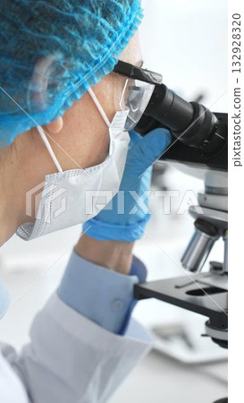 Female scientist in blue gloves and mask using microscope in laboratory setting, conducting important research and analysis, close-up. Medicine and science concept Female scientist in blue gloves and mask using microscope in laboratory setting, conducting important research and analysis, close-up. Medicine and science concept 132928320