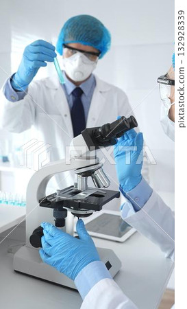 Two scientists, a man and a woman, in lab coats, masks and protective glasses conduct research with a microscope in a laboratory. Concept of medicine and science 132928339