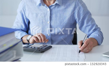 Financial professional calculating expenses, writing details next to laptop during budget analysis in corporate workspace. Audit and taxes in business Financial professional calculating expenses, writing details next to laptop during budget analysis in corporate workspace. Audit and taxes in business 132928343