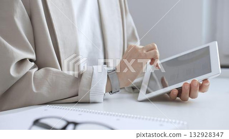 Professional woman working on tablet at desk, checking digital content with notebook and glasses nearby, focused on online tasks. Business people concept Professional woman working on tablet at desk, checking digital content with notebook and glasses nearby, focused on online tasks. Business people concept 132928347