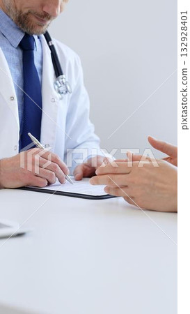 Unknown male doctor taking notes while listening to a female patient explaining her symptoms during a medical consultation in the clinic office. Medicine concept 132928401