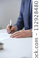 Closeup of businessman hands signing a contract with elegant pen, wearing a blue suit and a wristwatch, sitting at a white desk in office. Business people concept 132928480