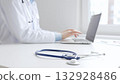 Closeup of blue stethoscope is lying on the table near female doctor working on laptop, highlighting digital tools transforming healthcare diagnostics and patient documentation. Medicine concept 132928486