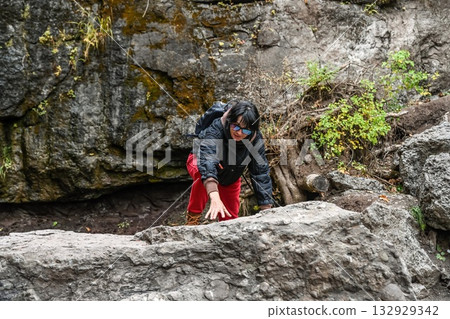 Active 50 year old Russian woman hiking in the mountains of Primorsky Krai, Russia. She climbs over rocks with a backpack, enjoying outdoor adventure. Active 50 year old Russian woman hiking in the mountains of Primorsky Krai, Russia. She climbs over rocks with a backpack, enjoying outdoor adventure. 132929342