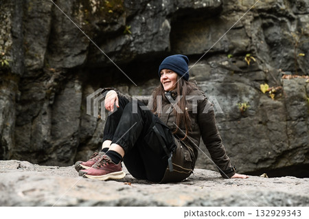 Russian woman traveler sitting on a rock near a waterfall. Autumn hike adventure in the mountains, enjoying nature and outdoor freedom. Russian woman traveler sitting on a rock near a waterfall. Autumn hike adventure in the mountains, enjoying nature and outdoor freedom. 132929343