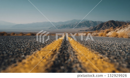 Desert Road with Yellow Lines Leading to Mountains Under Blue Sky 132929926