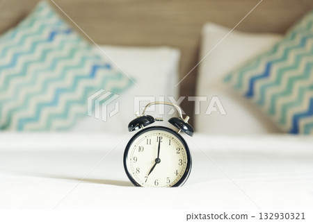 Hotel bedroom alarm clock on bed home interior cozy decoration room. Clean soft white bedsheet stylish decor relax dorm copy space. Alarm clock black vintage retro time white light Blurred background 132930321