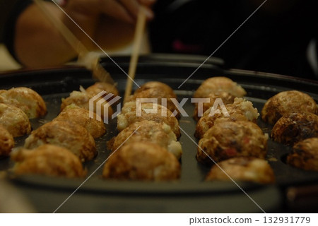 A sizzle shot of hot takoyaki being flipped over with chopsticks 132931779