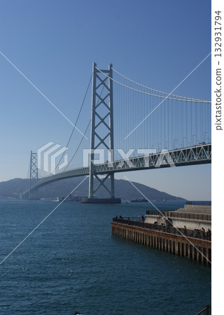 A wide-angle photo of a suspension bridge over a clear blue sea and clear skies 132931794