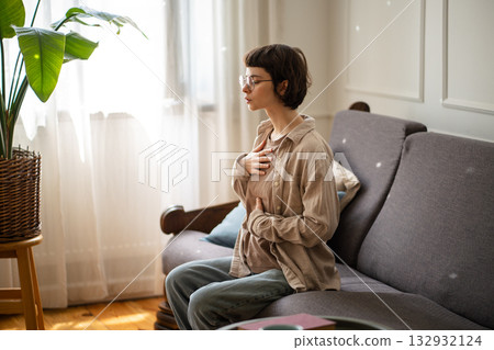 Meditating young woman with hands on chest practicing deep breaths to manage stress and anxiety 132932124
