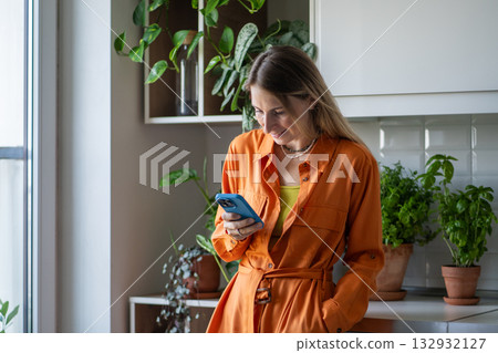 Laughing joyful woman with smartphone among kitchen herbs, sharing good news and shopping for plants 132932127