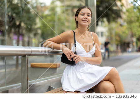 Positive young girl sitting at bus stop 132932346