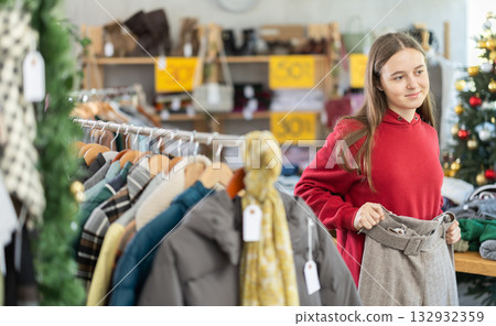 Teen girl is busy looking at clothes items in store, she choose trousers 132932359