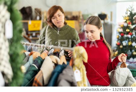 In sales area of store during Christmas sale, woman with teen daughter choose coat or jacket 132932385