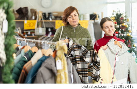 Adult woman and teenage girl choosing coat or down jacket Adult woman and teenage girl choosing coat or down jacket 132932412