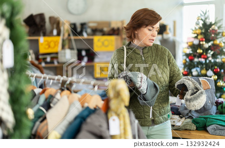 Adult woman chooses hat in clothing store Adult woman chooses hat in clothing store 132932424