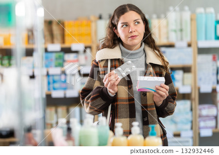 Young woman chooses pills at pharmacy Young woman chooses pills at pharmacy 132932446