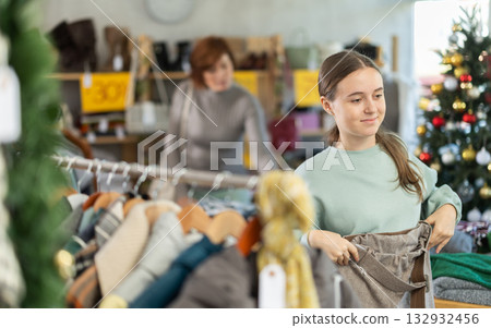 Teen girl is busy looking at clothes items in store, she choose trousers 132932456