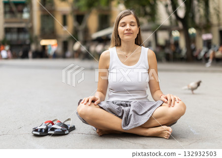 Woman in midst of bustle of city in pose of lotus asana 132932503