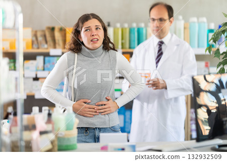 Woman suffering from stomach pain. Male pharmacist offering stomach pain pills Woman suffering from stomach pain. Male pharmacist offering stomach pain pills 132932509