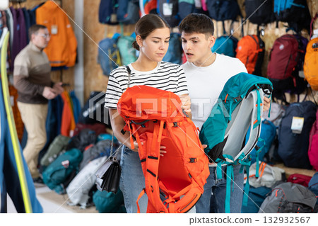 Young married couple chooses backpack for summer hike in tourist equipment store Young married couple chooses backpack for summer hike in tourist equipment store 132932567