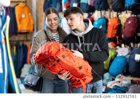 Young married couple in winter clothes chooses a durable backpack for a winter hike in tourist equipment store Young married couple in winter clothes chooses a durable backpack for a winter hike in tourist equipment store 132932581