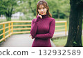 A woman in a knit dress smiling with her hand on her cheek 132932589
