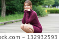 A woman in a burgundy knit dress squatting and smiling in the park 132932593
